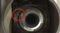 Very close-up view of the round drill chuck on the Perseverance rover with a tiny thread-like object circled in red.