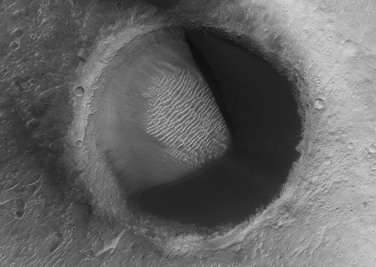 Round dune-filled crater with a dark shadow in the shape of Pac-Man.