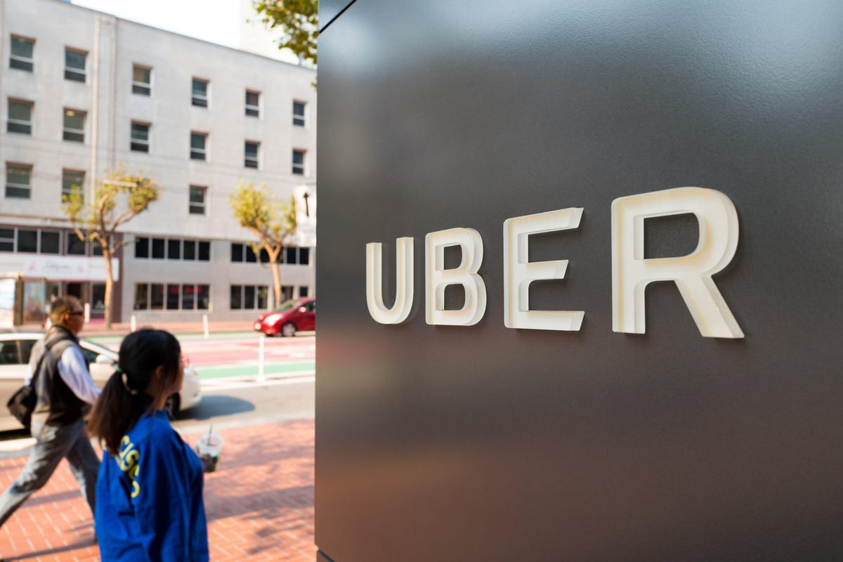 People walk down Market Street past sign with logo at the headquarters of ride-sharing technology company Uber in the South of Market (SoMa) neighborhood of San Francisco, California. Uber acknowledges it had a legal obligation to disclose a hack affectin