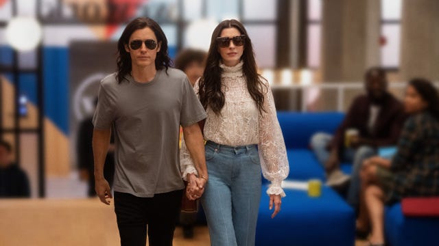 Jared Leto and Anne Hathaway wearing sunglasses, holding hands, walking through a building.