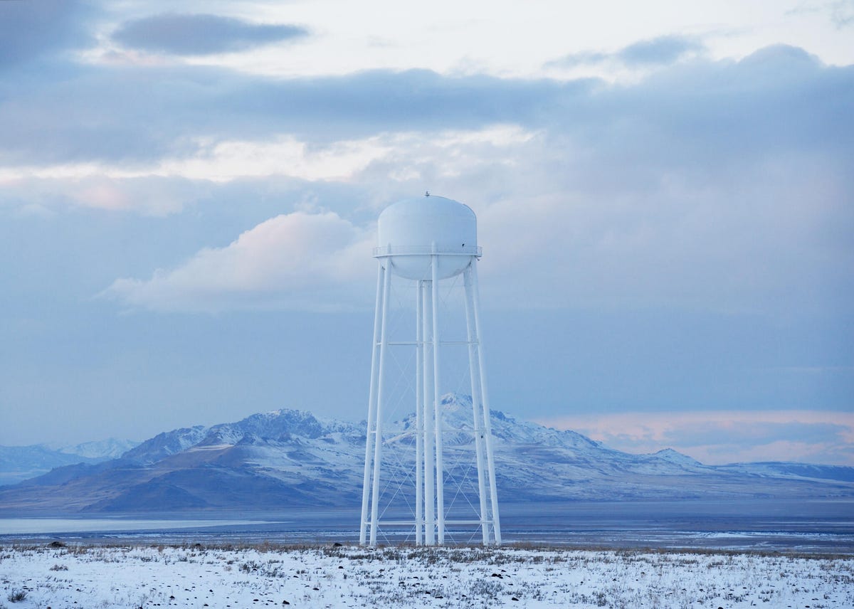 A white water tower in West Valley City, Utah, standing above a winter landscape with a mountain in the background.