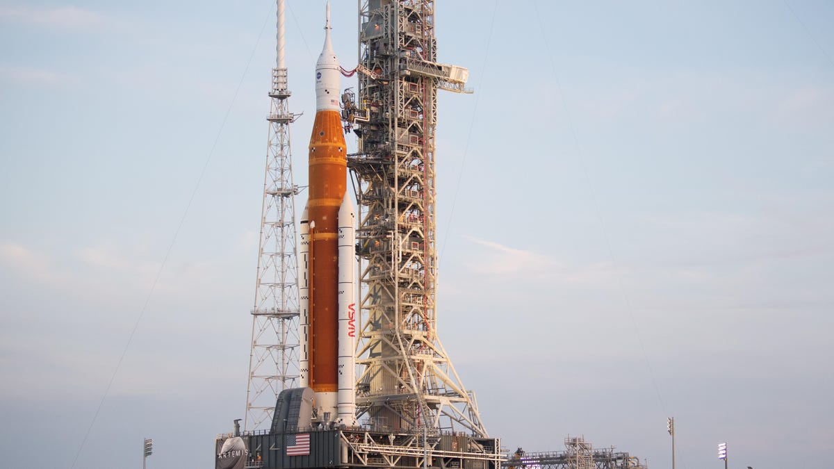 NASA's orange Artemis I rocket is seen atop the flame trench in the daytime.