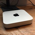 A close up of the silver Mac Mini on a wooden desktop.