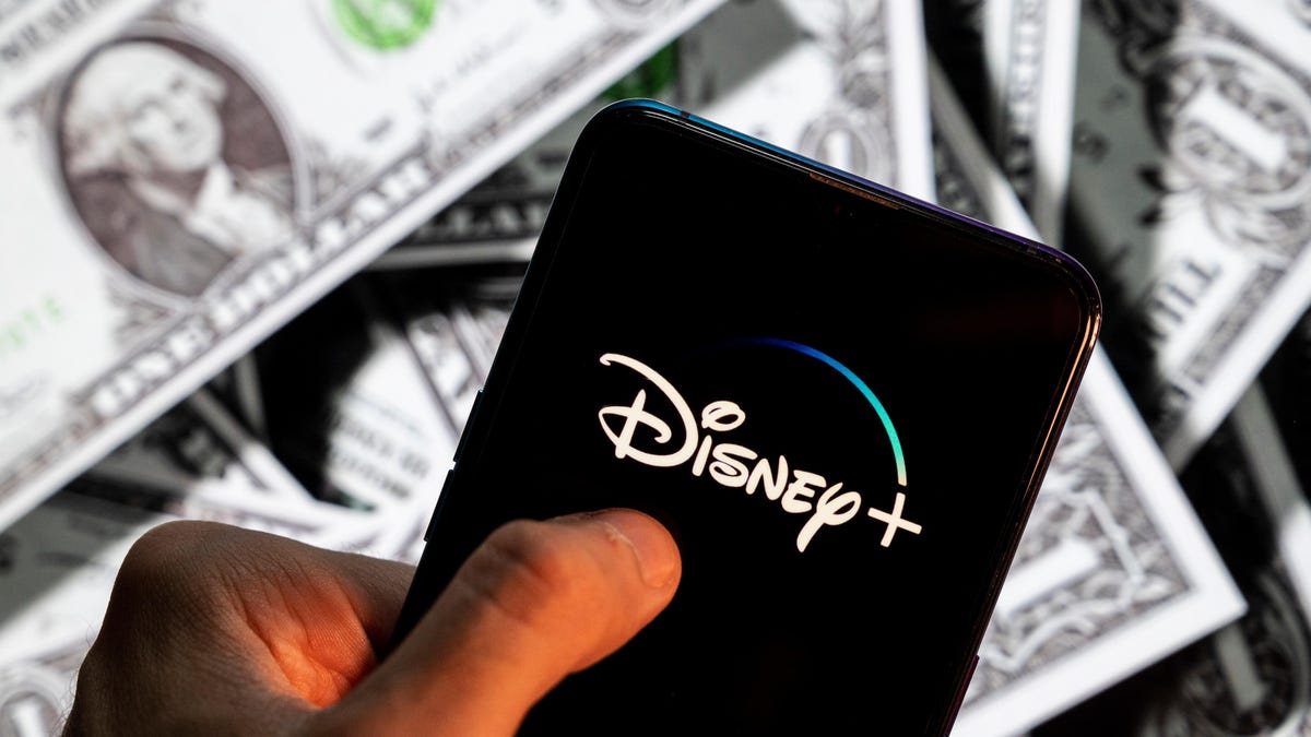 disney plus logo on phone hovering above pile of cash