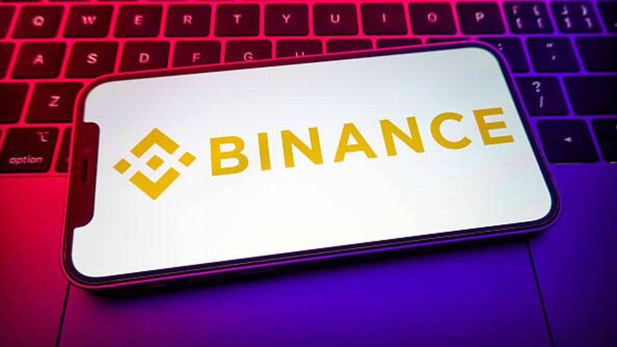Binance logo on a phone screen, with a computer keyboard in the background