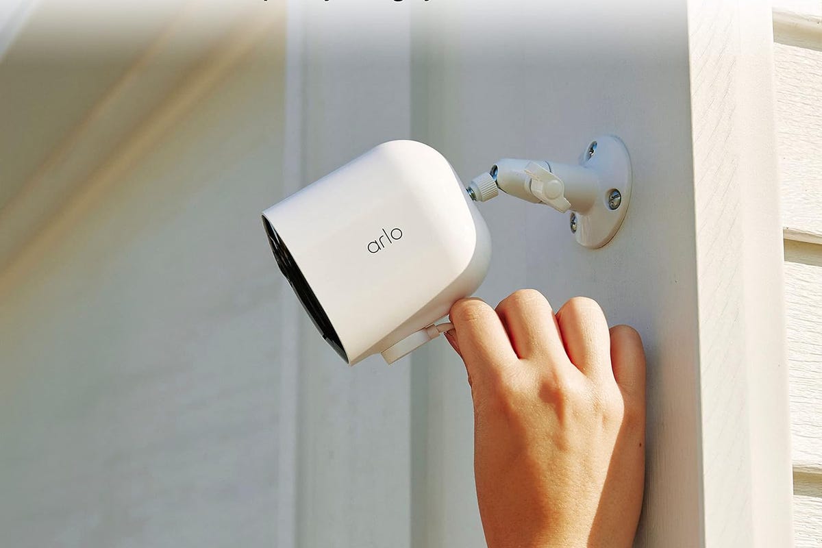 Una mano coloca la cámara Arlo Pro 5S 2K sobre un adorno blanco de exterior de una casa.