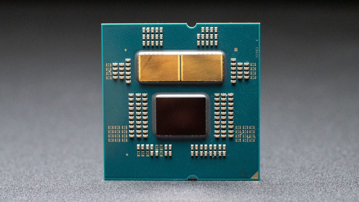 A closeup photo of an AMD Ryzen 7950X processor shows two golden-colored processor elements at the top and a darker one below
