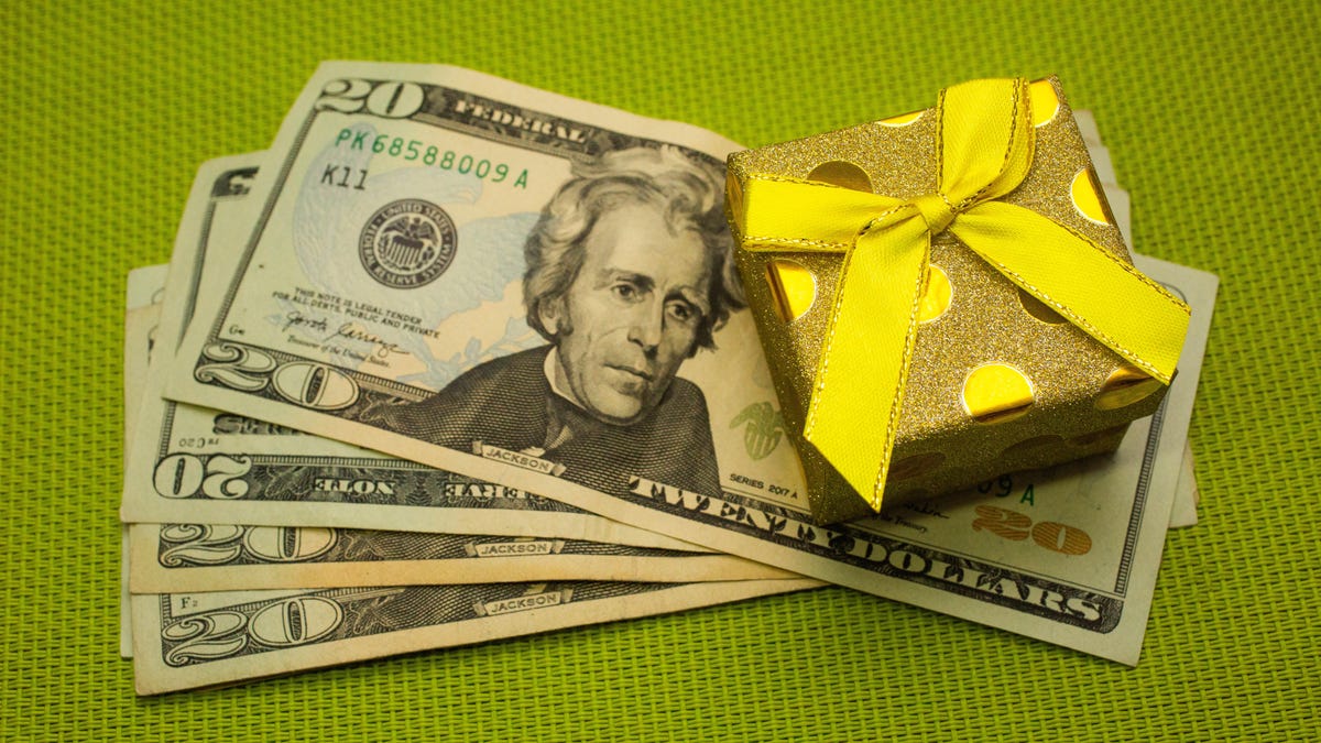 A stack of five $20 dollar bills with a small present with a yellow bow on top
