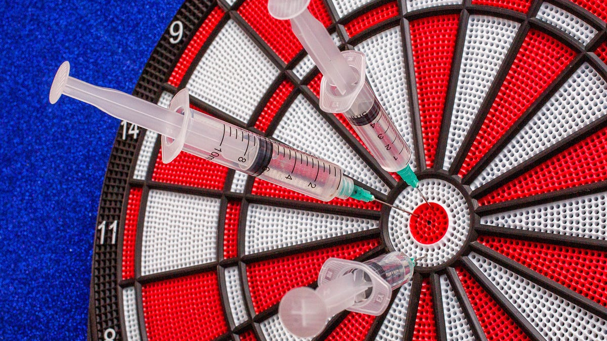A dartboard with three hypodermics stuck in the bull's-eye