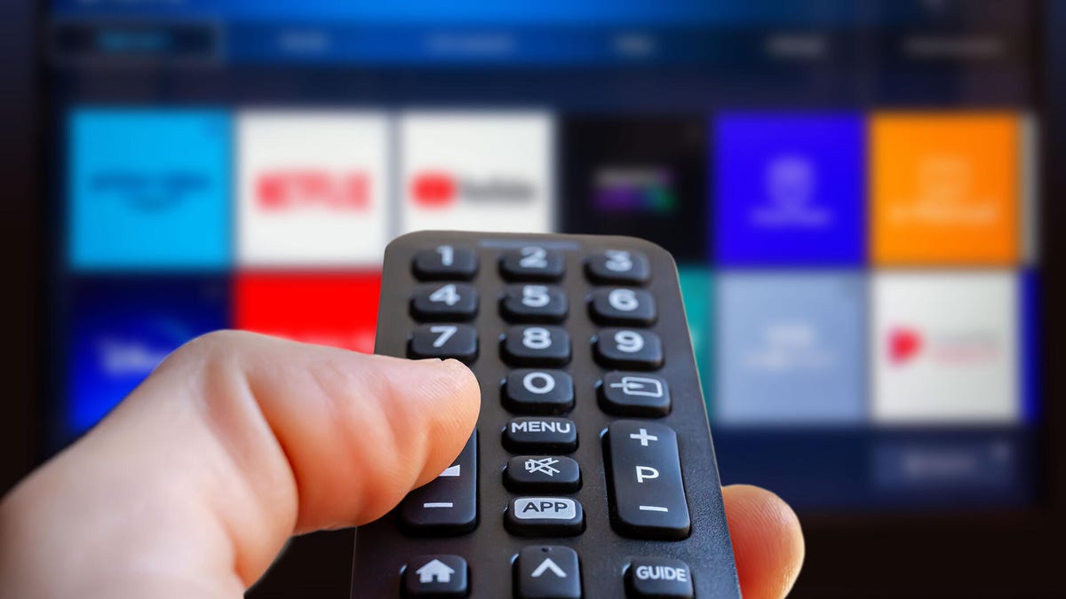 A hand on a remote with a smart TV interface in the background.