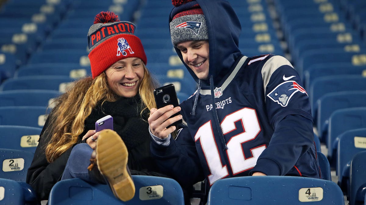 Two fans sit in a stadium looking at their phones