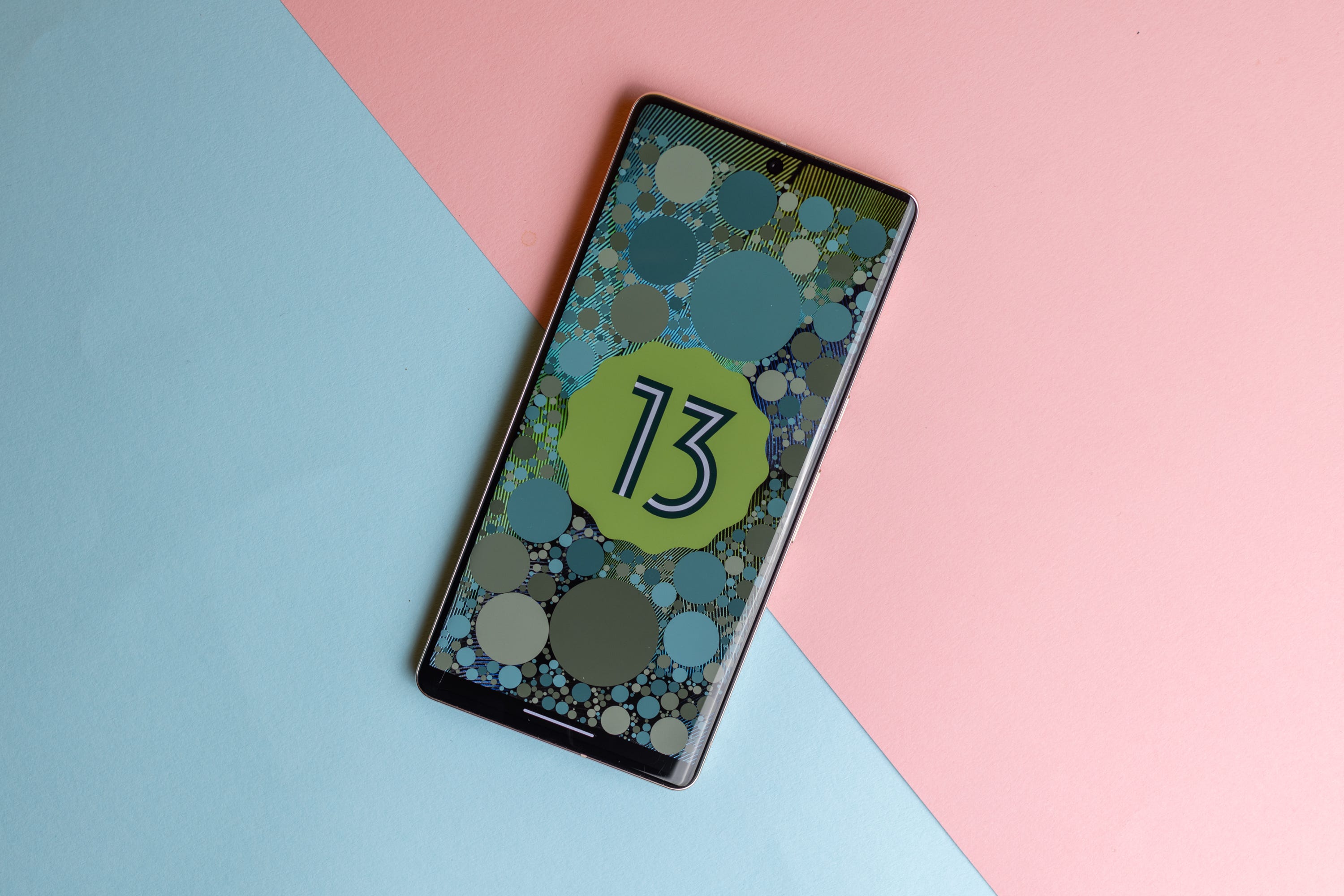Pixel 7 Pro phone with Android 13 logo on screen, on a blue and pink background