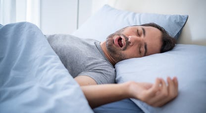 Man snoring while sleeping on bed.