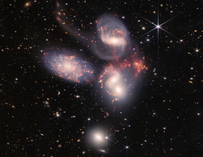 Galaxies of Stephan's Quintet sparkle against the background of space, within with distant galaxies are seen as little colorful specks.