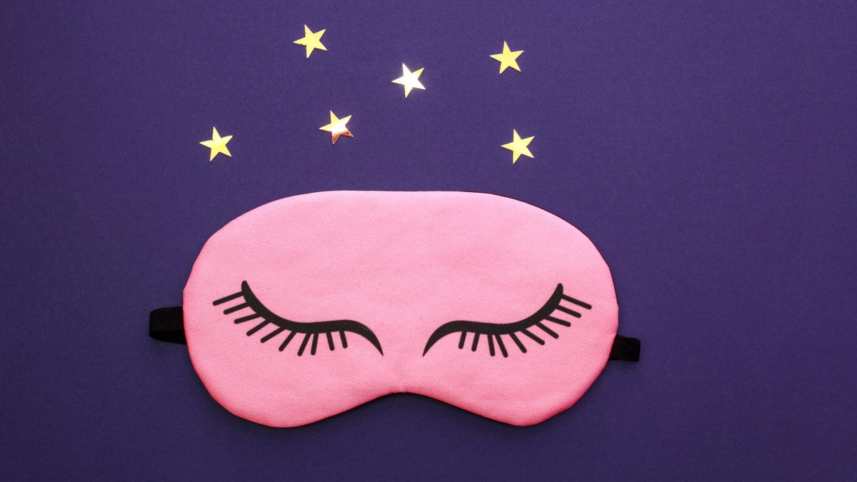 Pink sleep mask over dark purple background with gold stars.