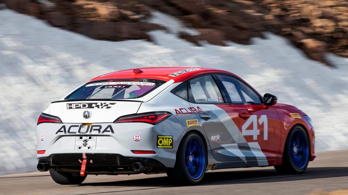 A white, gray and red 2023 Acura Integra driving past a snowy hillside at Pikes Peak.