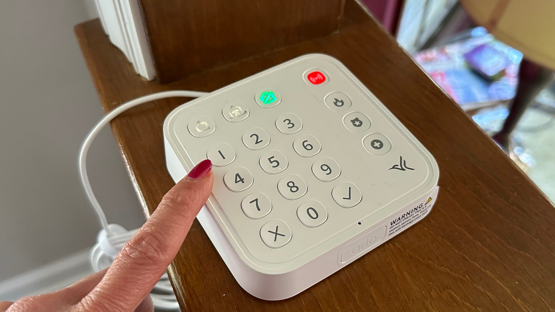 A woman's finger reaches to touch a button on the Arlo Home Security System's keypad hub.