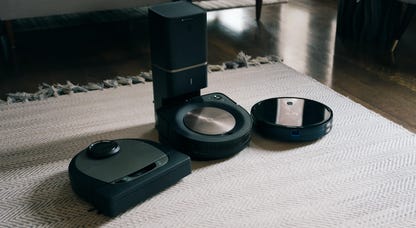 Three robot vacuum cleaners lined up on a white rug