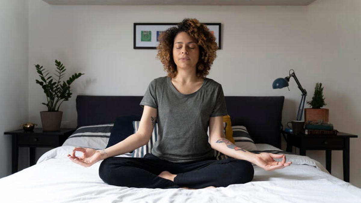 A woman meditating with crossed legs on a bed