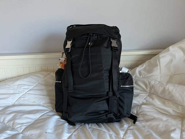 A black backpack sitting on a bed.