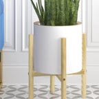 A ceramic pot planter with wooden frame filled with a plant sits near a chair.