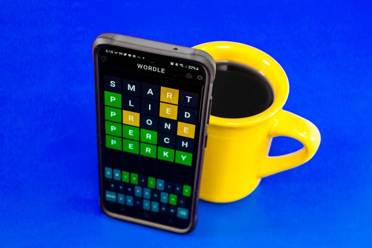 Wordle on a phone screen, next to a coffee cup
