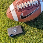 A black metal wallet on the grass with an American football next to it