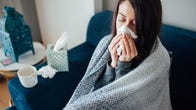 Woman with a cold sitting on couch and blowing her nose