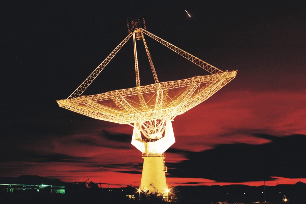 A large satellite dish is pointed toward a reddish sky during what appears to be late sunset.