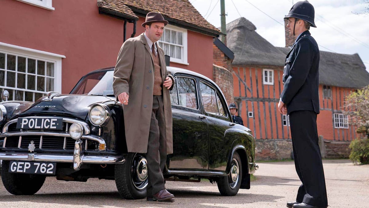 A detective leans against a 1950s car while talking to a cop in Magpie Murders