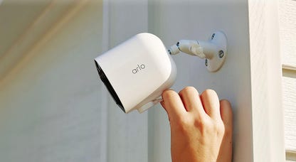 A hand reaches to adjust the Arlo Pro 5S 2K camera on white trim on the outside of the house.