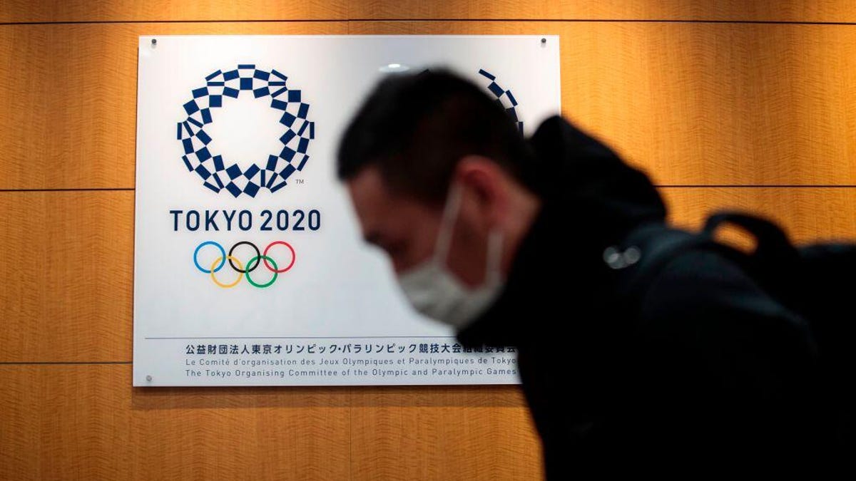 A man in a COVID mask walks by a Tokyo Olympics logo