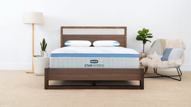 The Star Hybrid mattress from Bear on a wooden bed frame next to a lamp and chair.