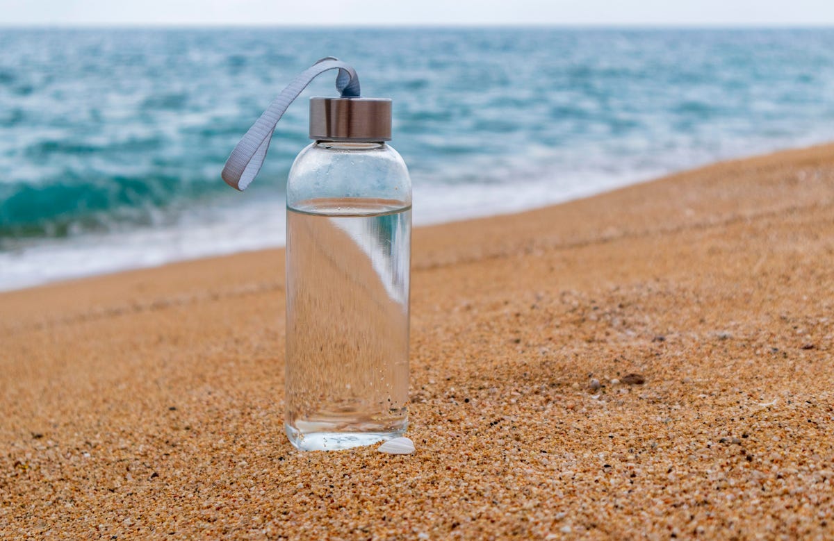 Γυάλινο μπουκάλι γεμάτο νερό στην παραλία με μεταλλικό πώμα