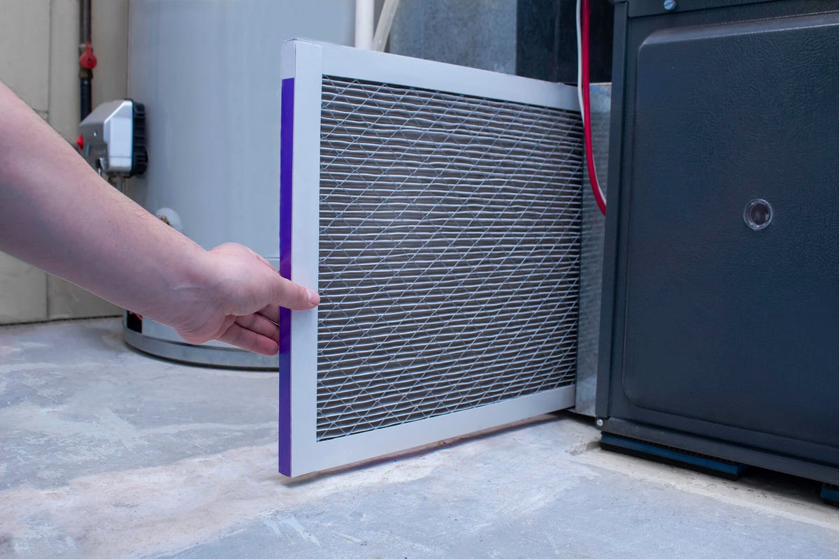 A person changing an air filter in a furnace, with a water heater in the background.