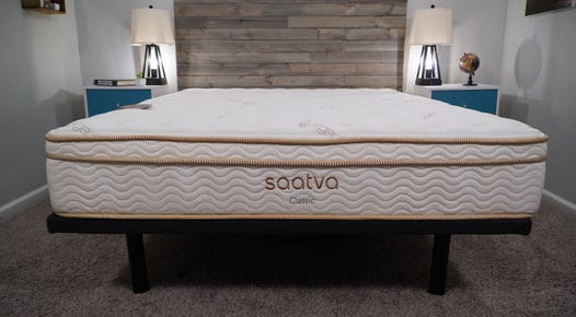 A Saatva Classic mattress on a standard black bed frame against a wooden backdrop
