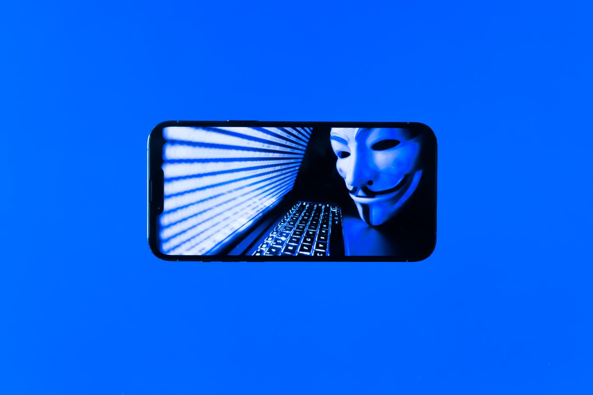 Image of a hacker wearing Anonymous mask on a phone