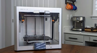 A silver 3D printer with plastic doors and two print heads