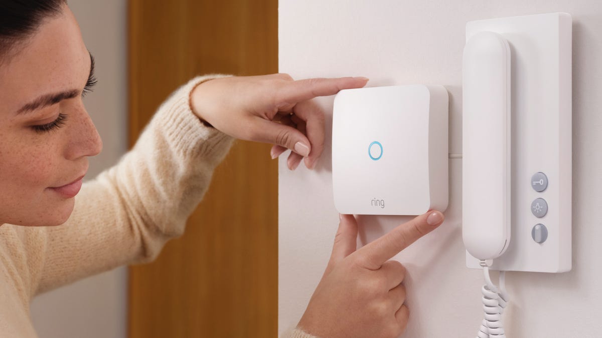 A woman installing the Ring Intercom on the wall of an apartment.