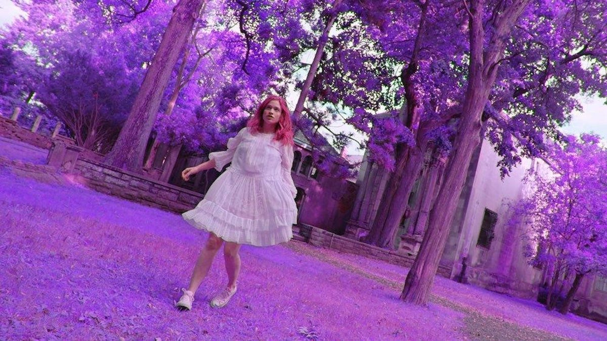A woman walks across a trippy purple lawn in the movie Braid.