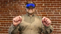 A man wearing an Apple Vision Pro headset holds his hands in front of him, with index fingers pressed against thumbs to control the software
