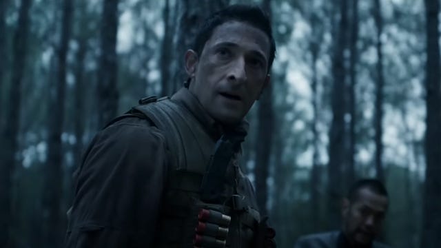 Adrien Brody in a forest looking at something off camera