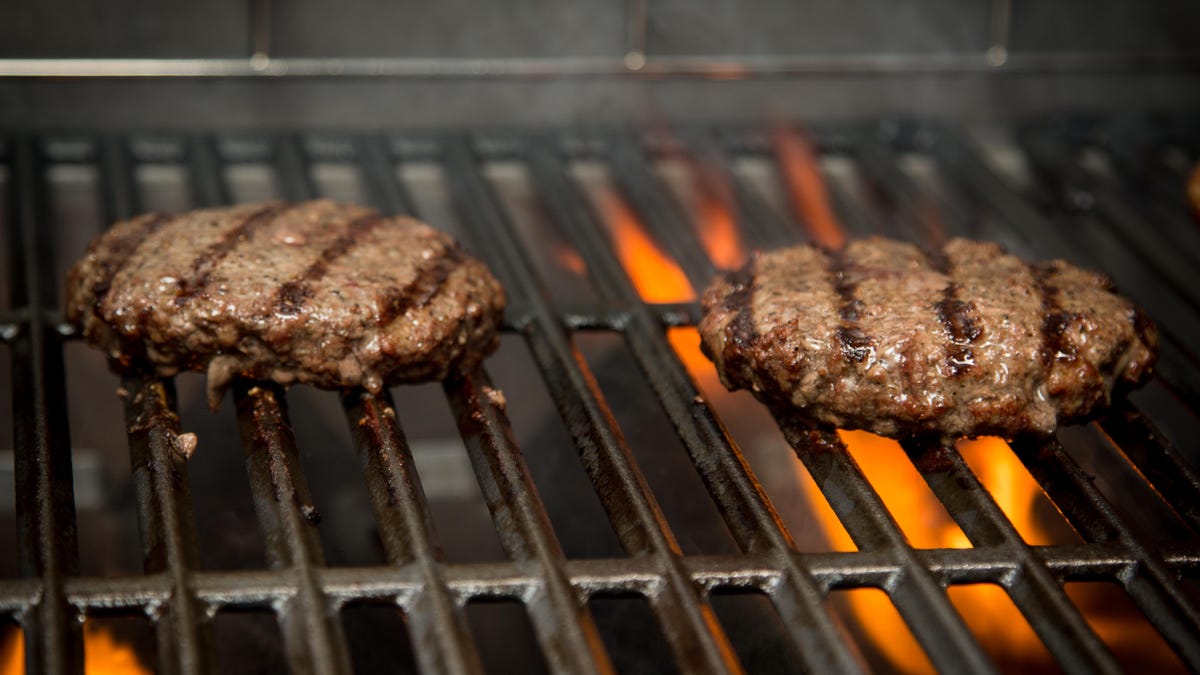 Two burger patties on a grill over flames