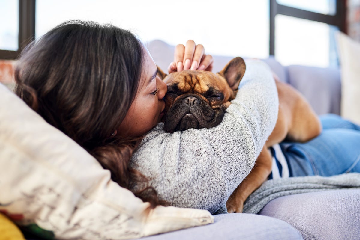 Woman lying on the couch hugging and kissing her dog.