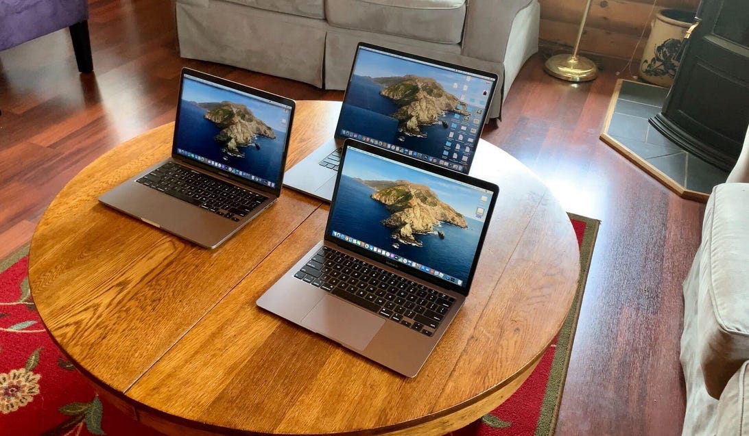 Three open MacBook laptops arranged on a wooden living room table.