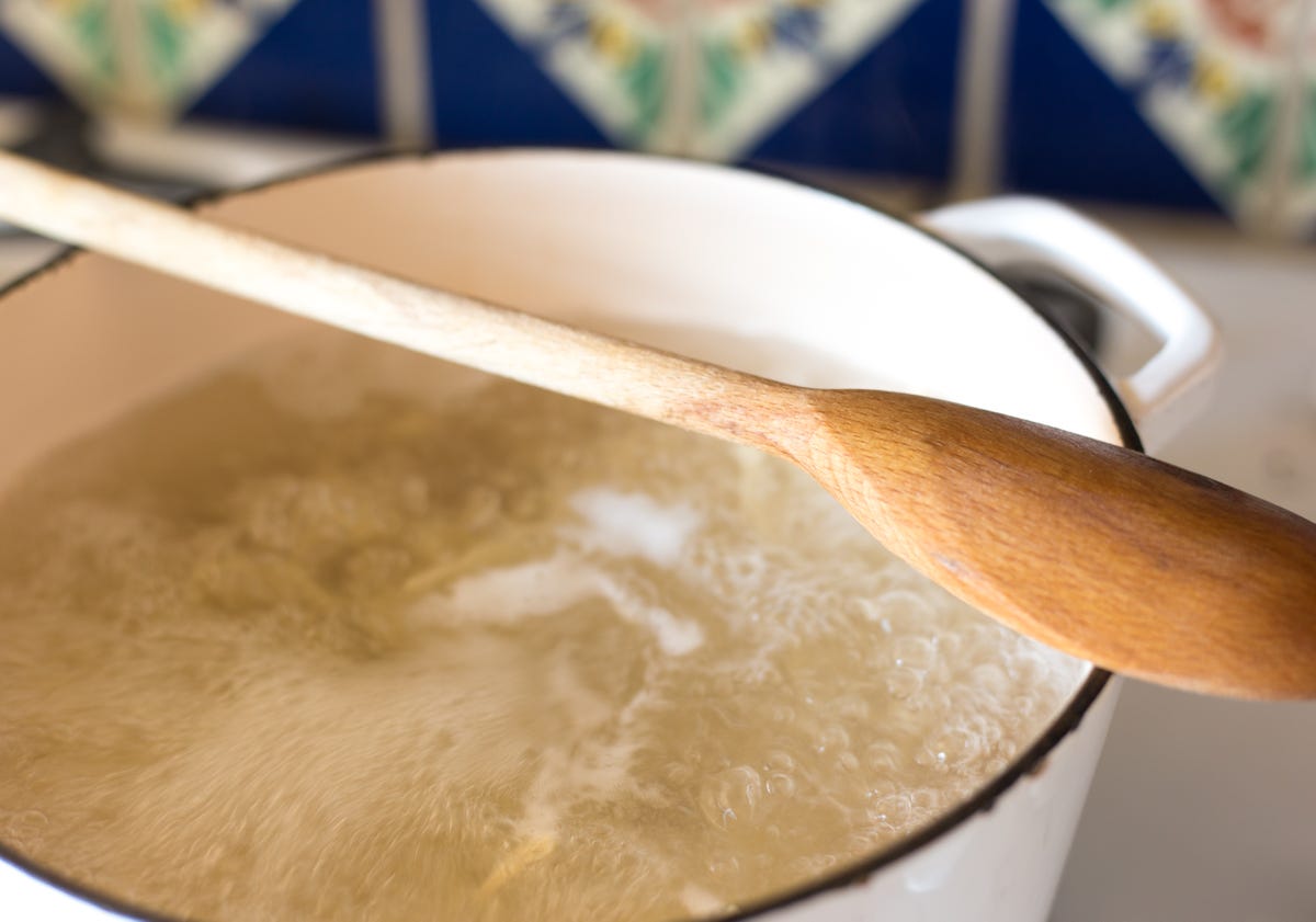 wooden spoon across pot of boiling water with pasta