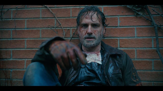 andrew lincoln as rick grimes sits against a brick wall with blood smear on his face