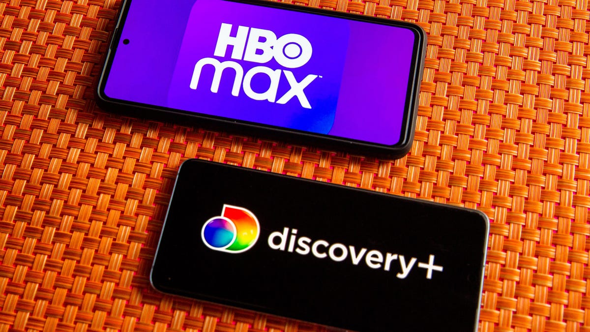 Two phones show the logos for HBO Max and Discovery Plus against an orange tablecloth