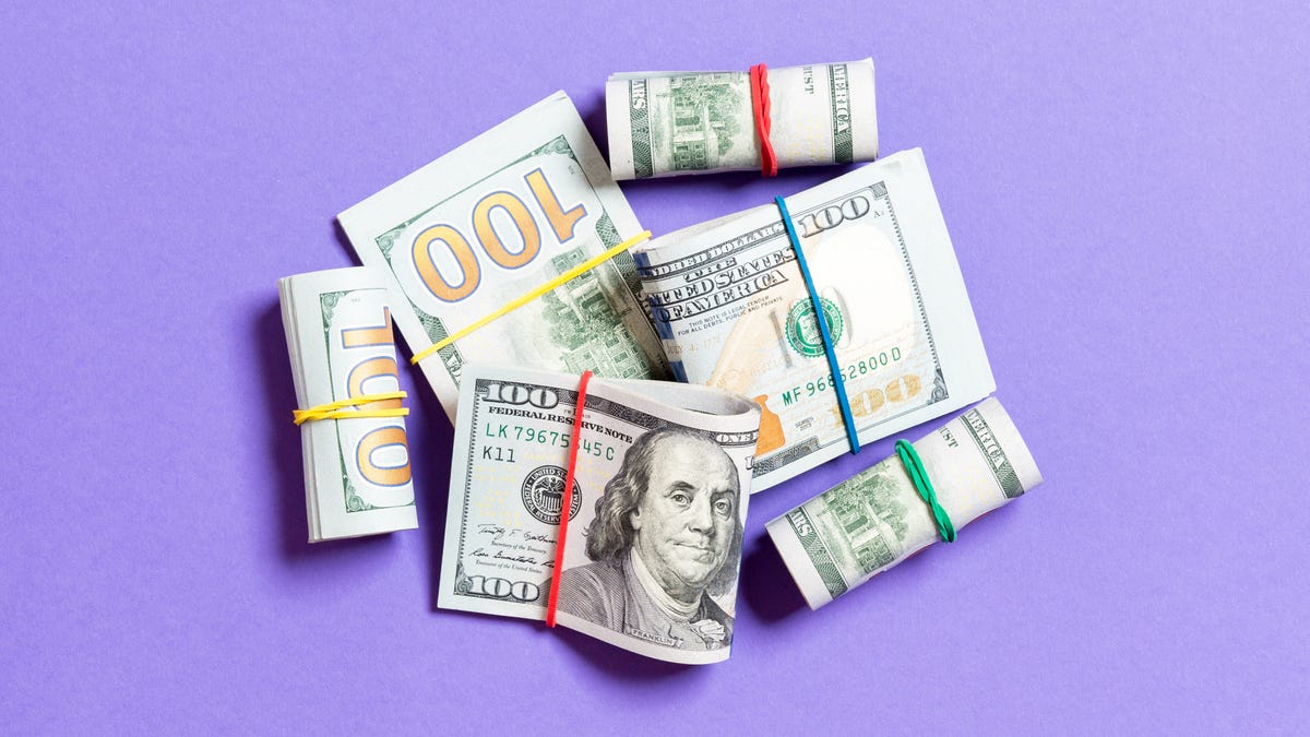 hundred dollar bills folded into bunches with rubber bands against purple background