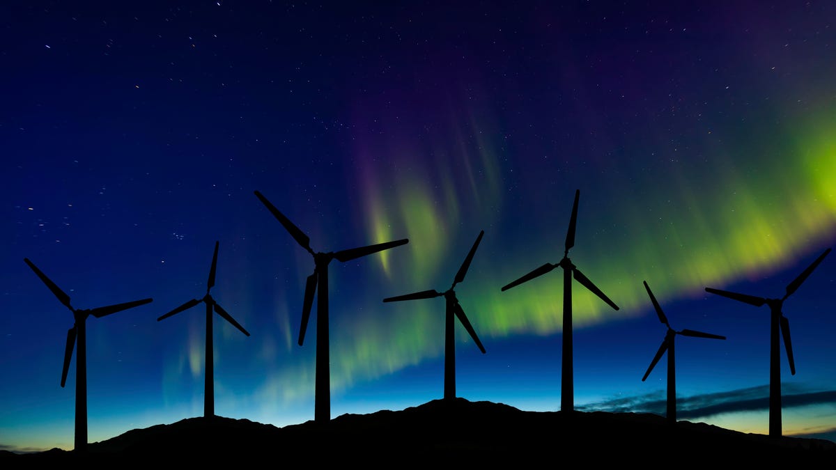 Wind turbines lit from behind by the northern lights.